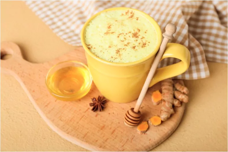 cup of healthy homemade turmeric latte with star anise and honey on color background