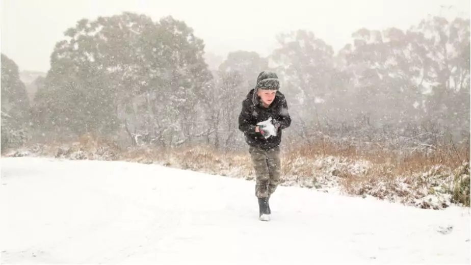 boy playing in fresh snow making snow balls during snow storm in new south wales