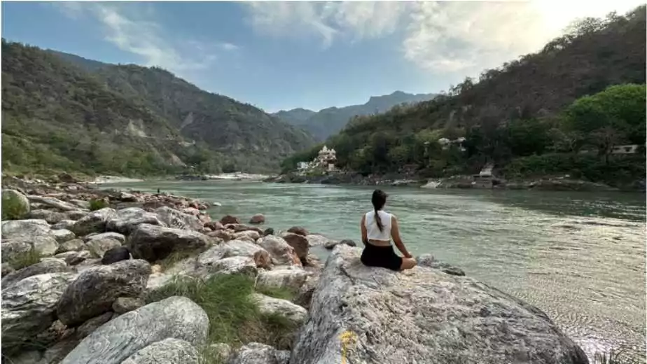 young girl sitting in lotos pose on big stone and doing meditation at sunrise time rishikesh