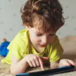 little cute boy in a green t shirt playing games on a tablet and watching cartoons