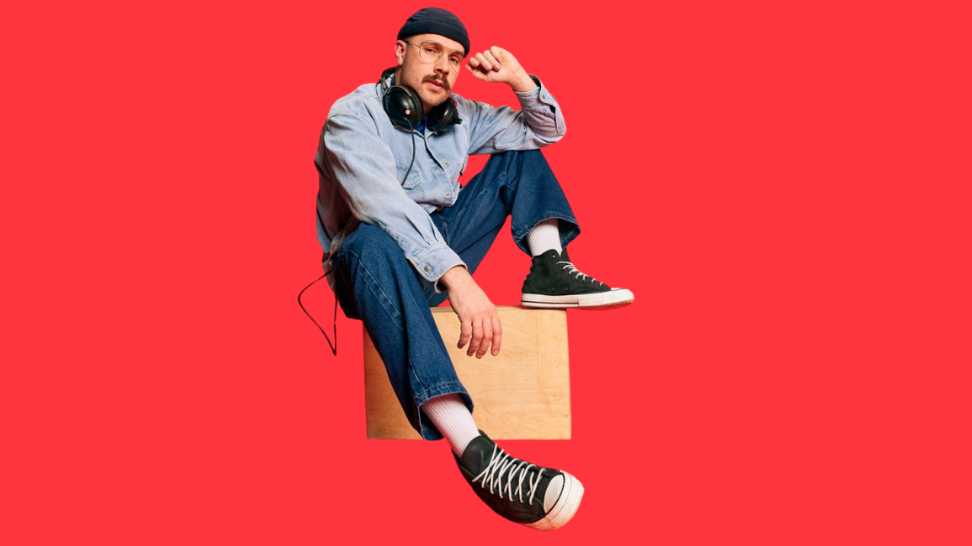 portrait of man in stylish clothes oversized jeans shirt hat and headphones posing over red background
